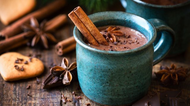 Hot-chocolate-with-a-cinnamon-stick-anise-star-and-grated- chocolate- topping-in-festive- Christmas- setting-on-dark-rustic-wooden- background-UNAMGlobal